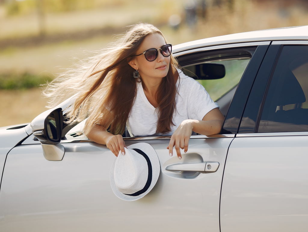Woman by the car. Lady in a white t-shirt. Famale in a white hat.